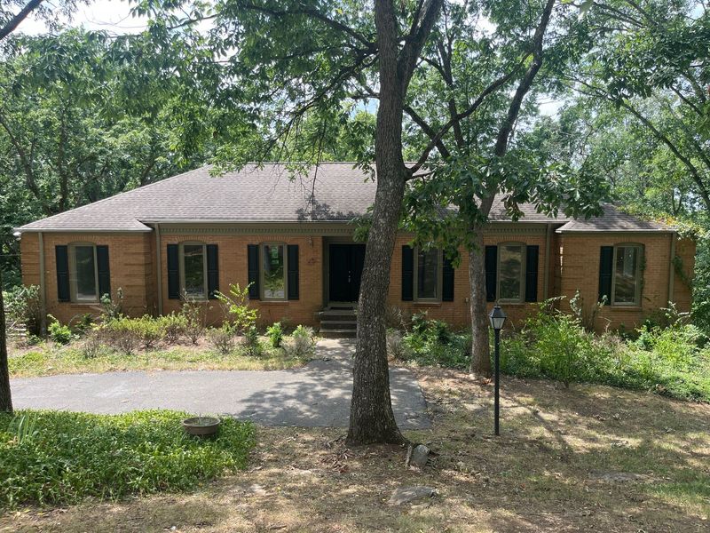 Alcott Dr exterior before — dated brick ranch with overgrown landscaping
