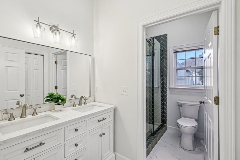 Windemere Woods bathroom after — marble floors, double vanity, glass shower with dark tile